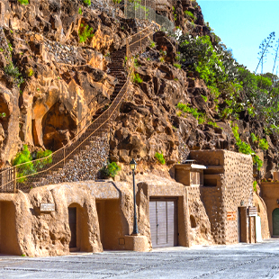Grotwoningen op Gran Canaria uitgehouwen in de rotsachtige bergwand, omringd door het droge en ruige landschap van het eiland.